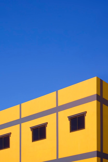 Glass windows on colorful yellow and purple house building wall against blue clear sky background