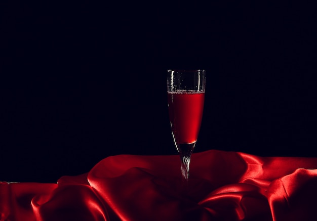 어두운 표면을 가진 빨간 실크에 와인 한 잔