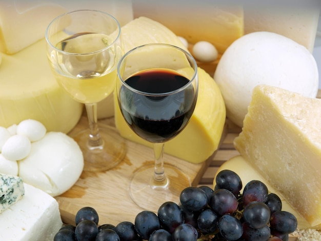 A glass of wine sits on a cutting board next to cheeses and other cheeses.