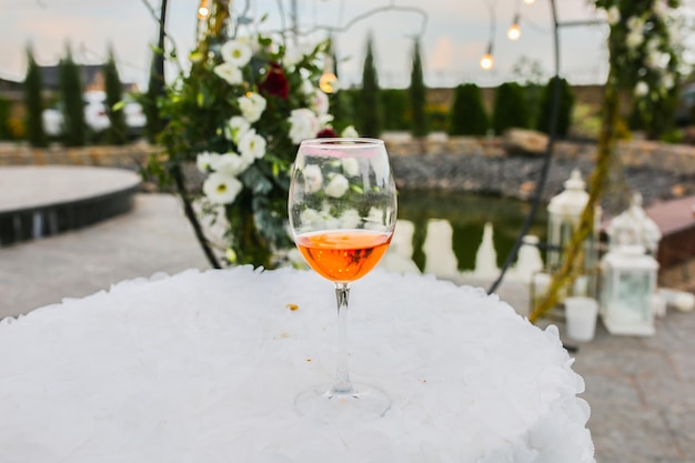 Bicchiere di vino in piedi sui tavolini all'aperto arco di fiori bianchi alla cerimonia di nozze sullo sfondo decorazione elegante