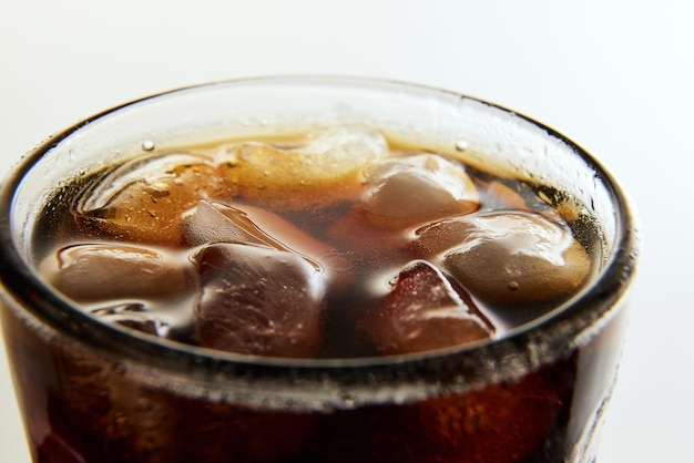 Glass wit foamy drink soda water coke dark beer with ice cubes against white background