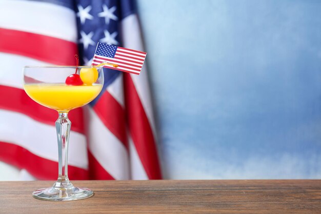 Glass with alcoholic cocktail on table against American flag background