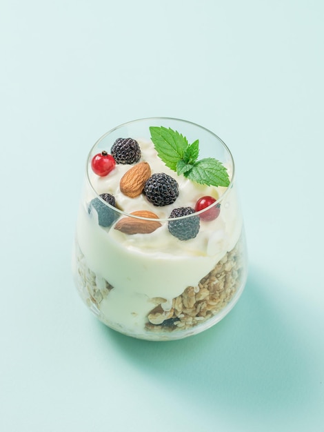 Glass with almonds berries granola and yogurt on a light blue background