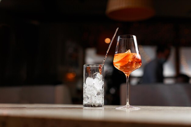 Glass with aperol cocktail and ice on bar counter