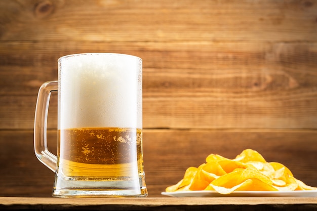 Glass with beer and chips on wooden wall.