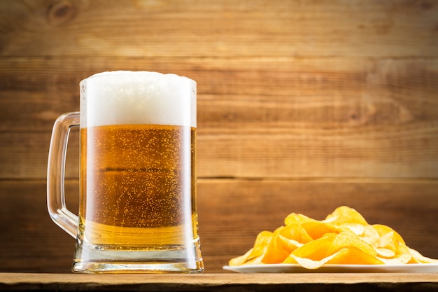 Glass with beer and chips on wooden wall.