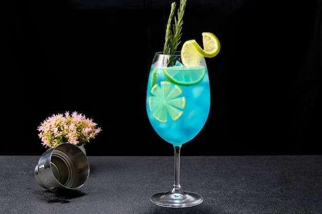 Glass with blue cocktail decorated with lemon and rosemary on dark background