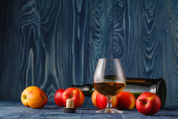 Glass with Calvados brandy and yellow apples on a wooden table