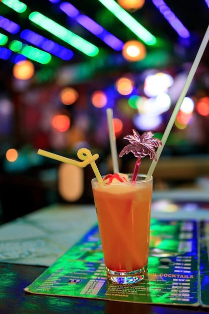 A glass with a cocktail and straws stands on the menu on the\
table in the bar with lights