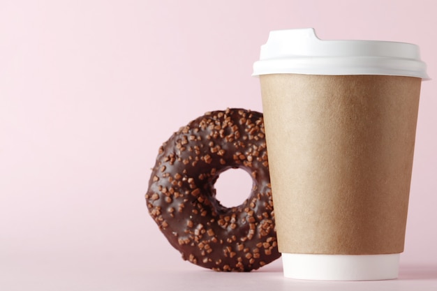 Glass with coffee and sweet tasty donut on a pink background with place for text.