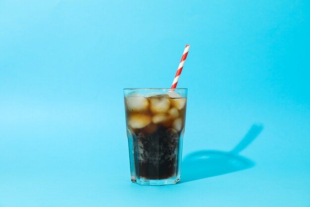 Glass with cold cola and tubule on blue background, space for text