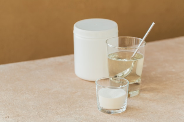 Glass with collagen dissolved in water and collagen protein powder on a light beige table.