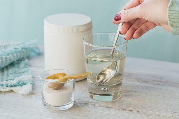 Glass with collagen dissolved in water and collagen protein powder on a white wooden table.