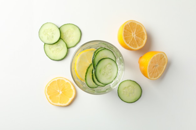 Glass with cucumber water, cucumber and lemon on white surface