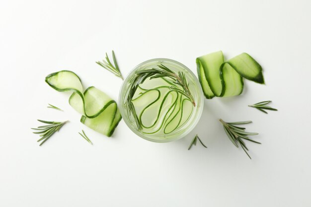 Glass with cucumber water and slices on white surface