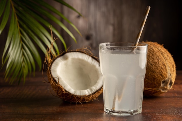 Glass with fresh coconut water and coconuts on the table