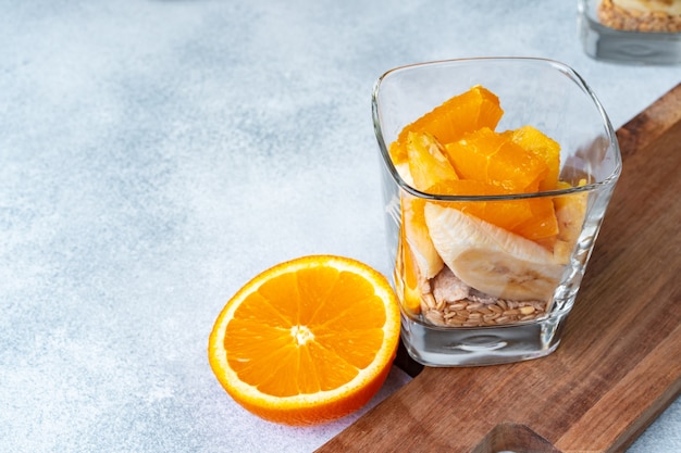 Glass with fruit pieces and oatmeal muesli on wooden board