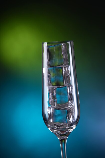 Glass with ice cubes on color background