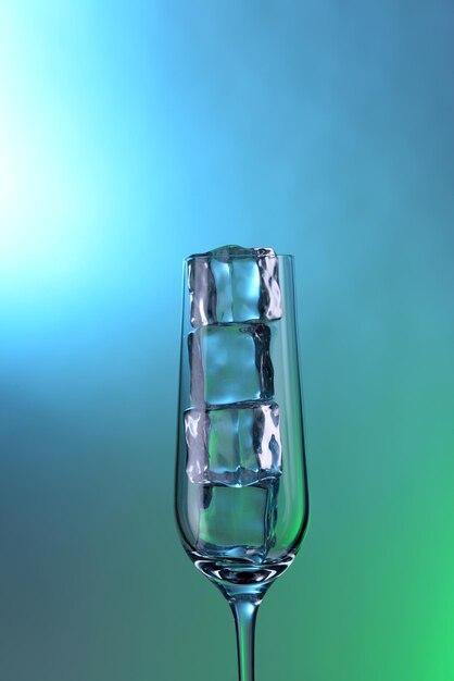 Glass with ice cubes on color background