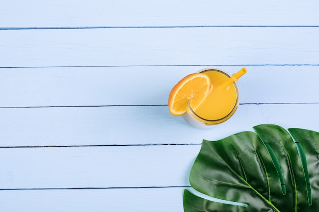 Photo glass with juice, monstera leaf on blue boards, copy space