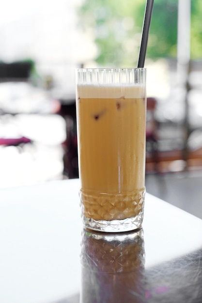 A glass with latte and black straws stands on a table with a metal coating on the summer terrace of a cafe Vertical photo