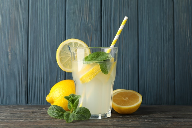 Glass with lemonade and lemons on wooden surface. Fresh drink