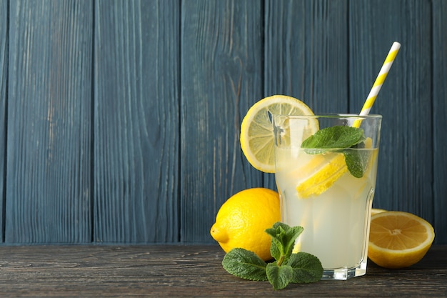 Glass with lemonade and lemons on wooden surface. Fresh drink