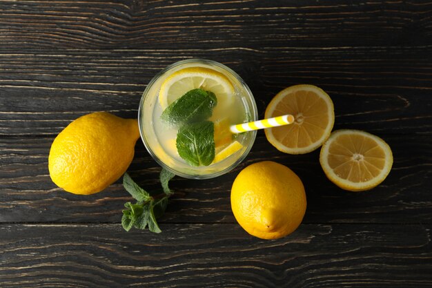 Glass with lemonade and lemons on wooden surface