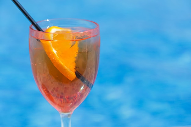 Vetro con cocktail d'arancia e fetta d'arancia contro l'acqua blu dello spazio della piscina per il testo