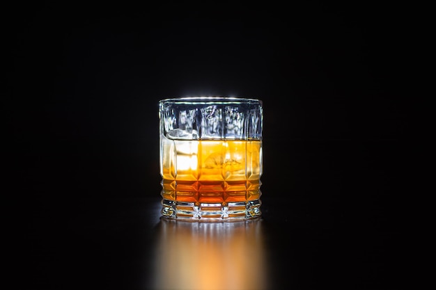 glass with orange drink with ice on table and black background