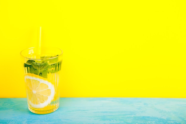 Glass with organic and fresh lemonade over yellow background on blue wooden board