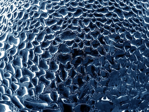 青いトーンの背景に雨滴の付いたガラス