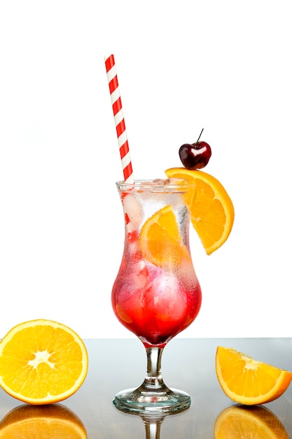 a glass with red cocktail decorated with orange and cherry with a straw inside the glass long dri