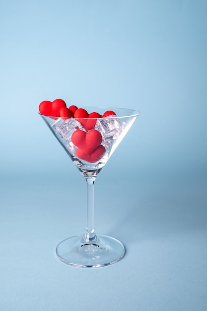 Glass with red heart shaped sugar candy and ice. Over blue background. Valentines Day, anniversary or wedding celebration concept. Copy space.