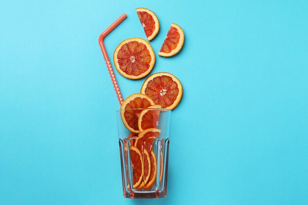 Glass with red orange slices and straw on blue isolated background