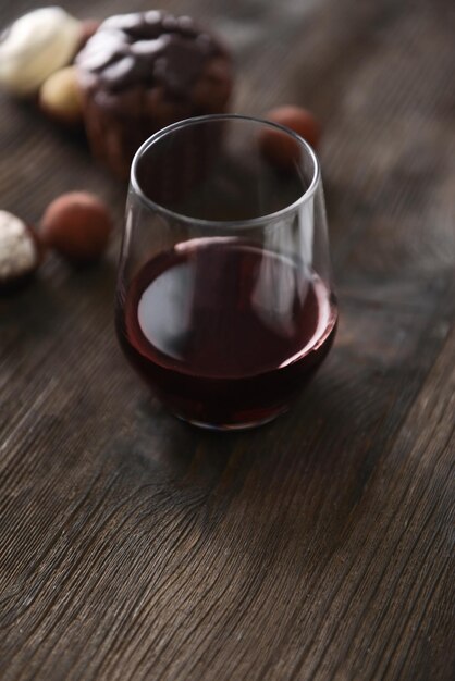 Foto bicchiere con vino rosso su tavola di legno e sfondo sfocato di deliziose caramelle al cioccolato