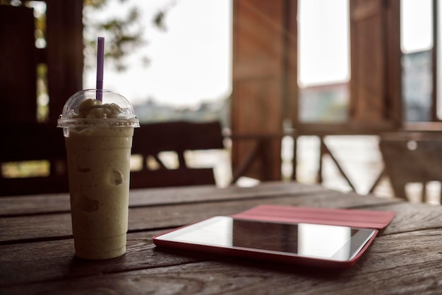 A glass with smoothies and a tablet on a wooden table on the veranda of a cafe