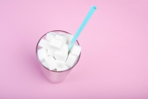 Glass with straw full of sugar cubes on pink. 