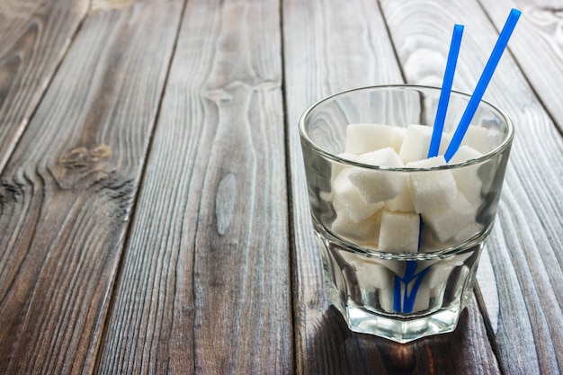 Glass with straw full of sugar and sugar cubes on wooden