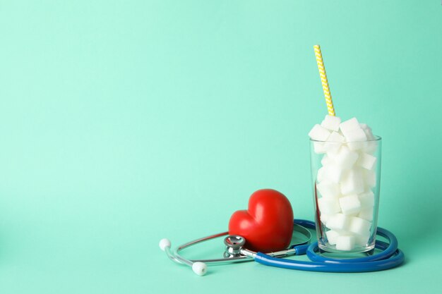 Glass with sugar cubes, heart and stethoscope on mint background