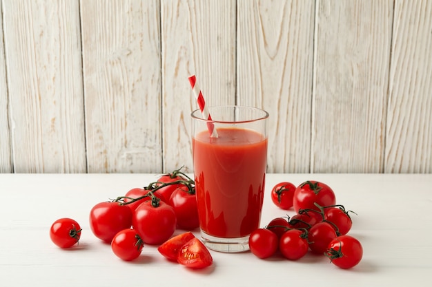 Glass with tomato juice and straw and tomatoes on wooden board