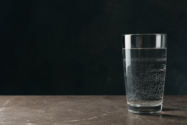 Glass with water on gray table, space for text