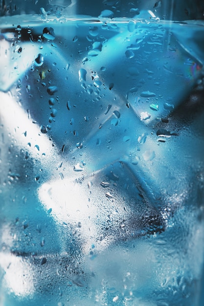 파란색 배경에 물과 얼음 조각이 있는 유리. 더운 무더운 날 구조 개념. 자유 공간