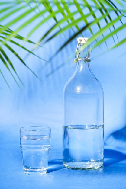 Glass with water near to bottle on blue surface