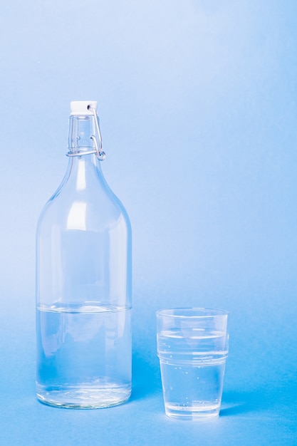 Glass with water near to bottle on blue