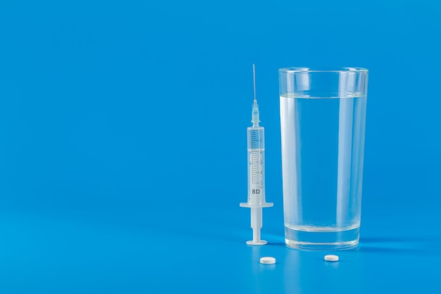 Glass with water and various pills isolated on blue background with copy space