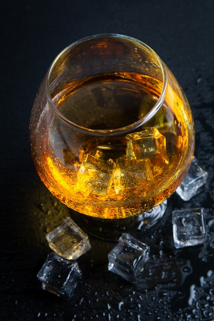 Glass with whiskey and ice on black table. Top view.