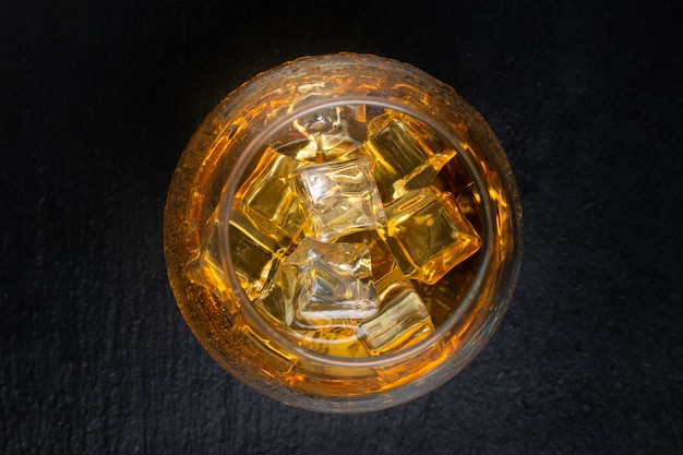 Glass with whiskey and ice on black table. Top view.