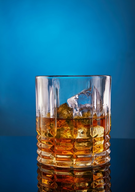 グラデーションと反射のブルーテーブルにウイスキーと氷のグラス