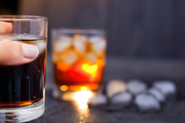 Glass with whiskey or rum with cola with ice in hand on a dark background